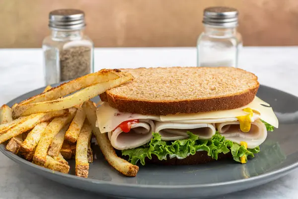 Marul ve peynirli dilimlenmiş hindi, yanında patates kızartması ve buğday ekmeği ile servis ediliyor.