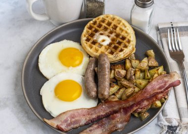 Erimiş tereyağlı kızarmış yumurta, domuz pastırması, sosis ve patates kızartması ile servis edilen şurup.
