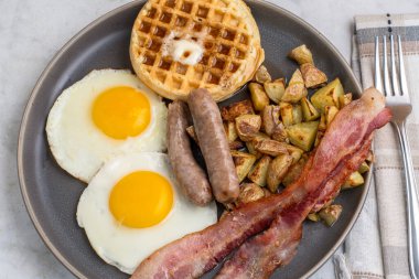 Erimiş tereyağlı kızarmış yumurta, domuz pastırması, sosis ve patates kızartması ile servis edilen şurup.