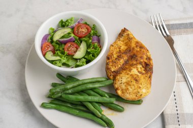 Baharatlı tavuk göğsü, salata ve yeşil fasulye ile servis edilir..