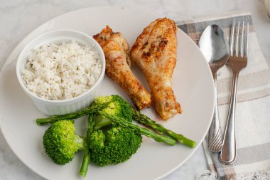 Brokoli ve aspaagusla servis edilen tavuk budu ve pilav.