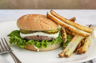  Peynirli ve turşulu hamburger üstü, patates kızartmasıyla servis edilen susamlı ekmek.