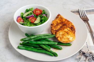 Baharatlı tavuk göğsü, salata ve yeşil fasulye ile servis edilir..