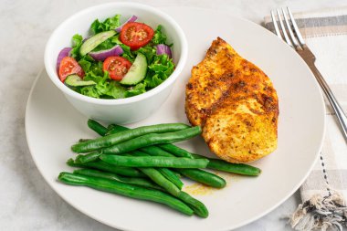 Baharatlı tavuk göğsü, salata ve yeşil fasulye ile servis edilir..