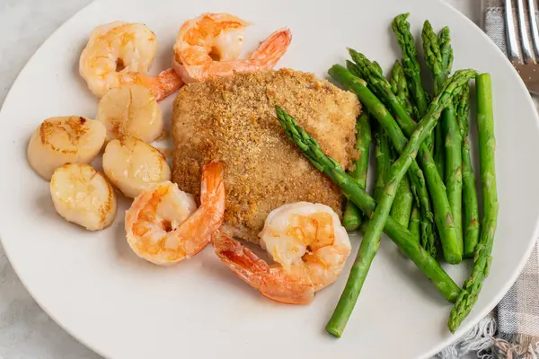 Fırında mezgit ve istiridye ve karides ile servis edilen kuşkonmaz.