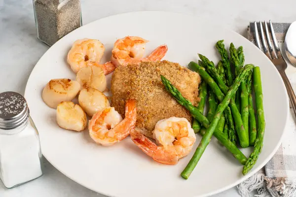 Fırında mezgit ve istiridye ve karides ile servis edilen kuşkonmaz.