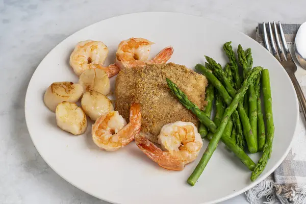 Fırında mezgit ve istiridye ve karides ile servis edilen kuşkonmaz.