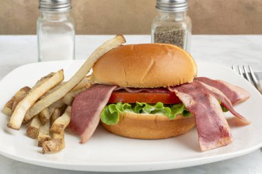 hindi pastırmalı marul ve domatesli çörek ve yanında patates kızartması.