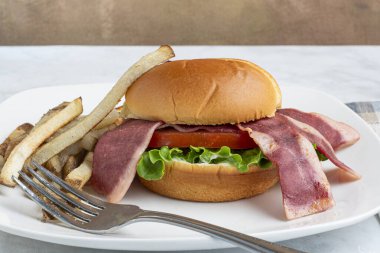 hindi pastırmalı marul ve domatesli çörek ve yanında patates kızartması.