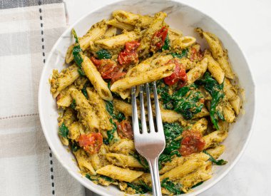 Pesto ile karıştırılmış makarna sotelenmiş domatesle servis ediliyor.