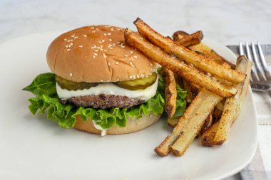  Peynirli ve turşulu hamburger üstü, patates kızartmasıyla servis edilen susamlı ekmek.