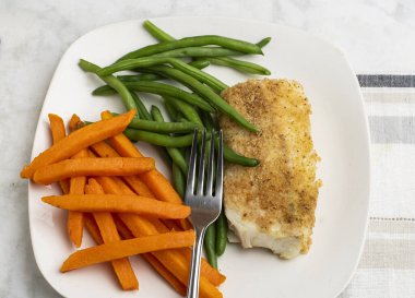  Tatlı patates kızartması ve taze fasulyeyle servis edilen kızarmış morina balığı.