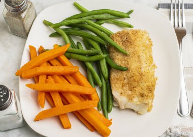  Tatlı patates kızartması ve taze fasulyeyle servis edilen kızarmış morina balığı.