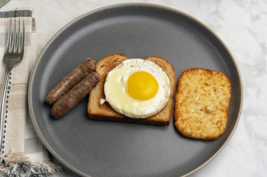 Kızarmış yumurtalı tost, yanında sosis ve patates kızartması.