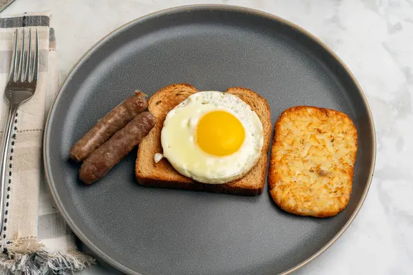 Kızarmış yumurtalı tost, yanında sosis ve patates kızartması.