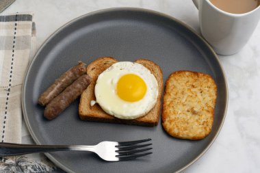 Kızarmış yumurtalı tost, yanında sosis ve patates kızartması.