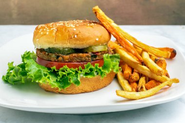 Bahçe sebzeli burger, domates, marul ve turşulu susamlı ekmek ve yanında patates kızartması.