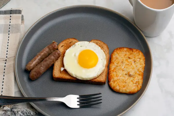 Kızarmış yumurtalı tost, yanında sosis ve patates kızartması.