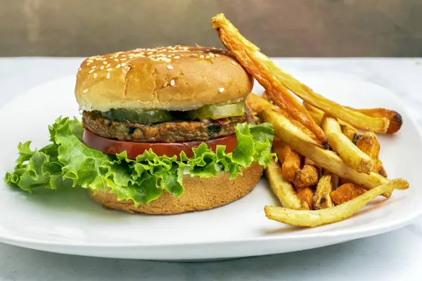Bahçe sebzeli burger, domates, marul ve turşulu susamlı ekmek ve yanında patates kızartması.