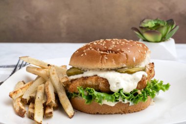  Turşu ve mayonez ile patates kızartması ile servis edilen balıklı fileto sandviç.