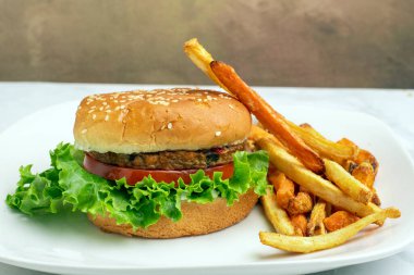 Bahçe sebzeli burger, domates, marul ve turşulu susamlı ekmek ve yanında patates kızartması.