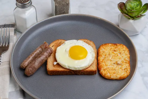 Kızarmış yumurtalı tost, yanında sosis ve patates kızartması.
