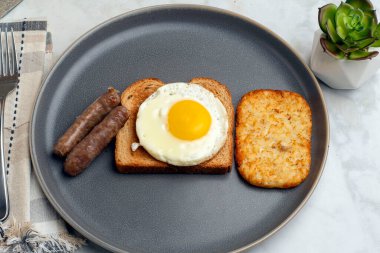 Kızarmış yumurtalı tost, yanında sosis ve patates kızartması.