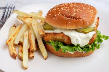  Turşu ve mayonez ile patates kızartması ile servis edilen balıklı fileto sandviç.