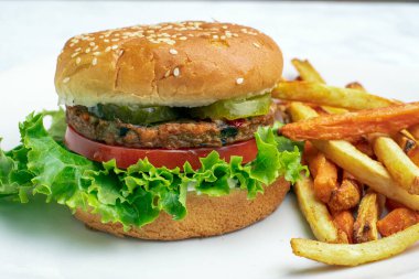 Bahçe sebzeli burger, domates, marul ve turşulu susamlı ekmek ve yanında patates kızartması.