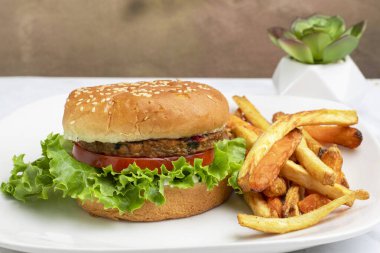 Bahçe sebzeli burger, domates, marul ve turşulu susamlı ekmek ve yanında patates kızartması.