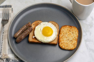 Kızarmış yumurtalı tost, yanında sosis ve patates kızartması.