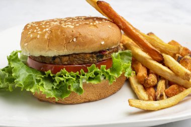 Bahçe sebzeli burger, domates, marul ve turşulu susamlı ekmek ve yanında patates kızartması.
