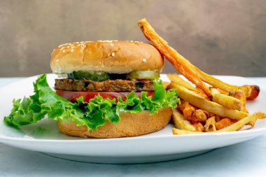 Bahçe sebzeli burger, domates, marul ve turşulu susamlı ekmek ve yanında patates kızartması.