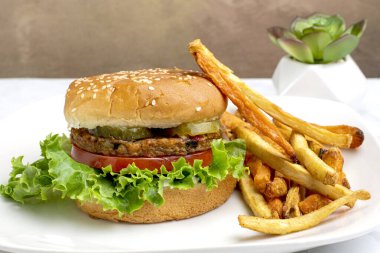 Bahçe sebzeli burger, domates, marul ve turşulu susamlı ekmek ve yanında patates kızartması.