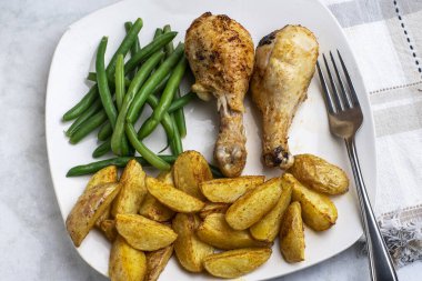 Yeşil fasulye ve patates dilimleri ile servis edilen tavuk budu.