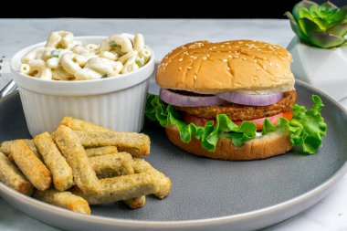 Bahçe burgerinin üstünde kırmızı soğan ve makarna salatası var.