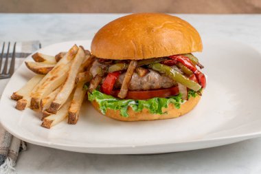 Ev yapımı patates kızartmasıyla hazırlanmış brioche çöreği üzerine sotelenmiş biber ve soğan soslu auasage burger üstü.