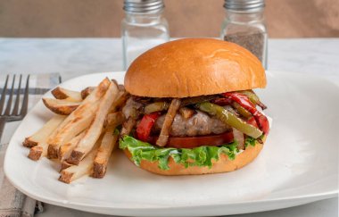 Ev yapımı patates kızartmasıyla hazırlanmış brioche çöreği üzerine sotelenmiş biber ve soğan soslu auasage burger üstü.