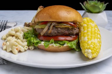  Mısır, friess ve makarna salatalı abur cuburla servis edilen soğan ve biberli hamburger tepesi.