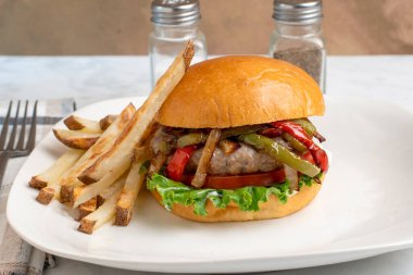 Ev yapımı patates kızartmasıyla hazırlanmış brioche çöreği üzerine sotelenmiş biber ve soğan soslu auasage burger üstü.