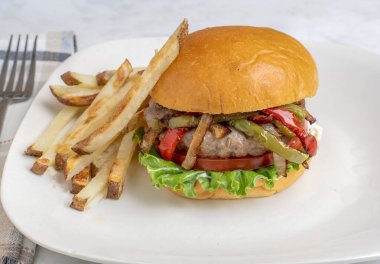 Ev yapımı patates kızartmasıyla hazırlanmış brioche çöreği üzerine sotelenmiş biber ve soğan soslu auasage burger üstü.