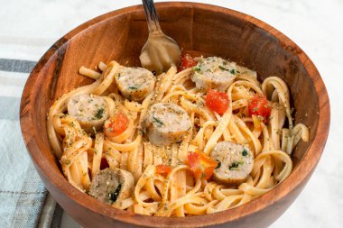 Tavuk sosisi ve doğranmış domatesle servis edilen makarna.