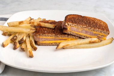 Ev yapımı patates kızartmasıyla servis edilen jambonlu sandviç., 