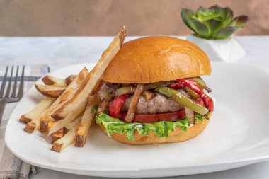 Ev yapımı patates kızartmasıyla hazırlanmış brioche çöreği üzerine sotelenmiş biber ve soğan soslu auasage burger üstü.