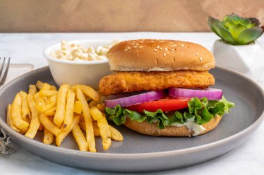 Makarna salatası ve patates kızartmasıyla servis edilen susamlı ekmeğin üzerine soğanlı tavuk filetosu ve domates.