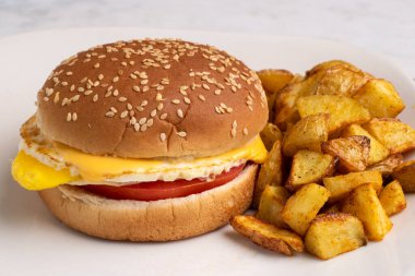 Kızarmış yumurta ve peynirli domatesli susamlı çörek ve patates kızartması.