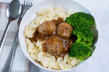 Patates püresi ve brokoli ile servis edilen soslu İtalyan usulü köfteler.