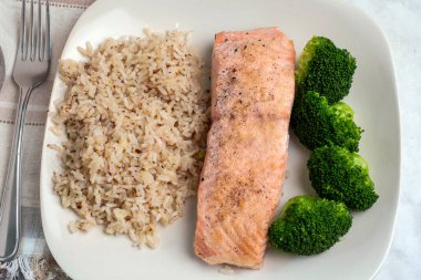 Makarna salatası ve patates kızartmasıyla servis edilen susamlı ekmeğin üzerine soğanlı tavuk filetosu ve domates.