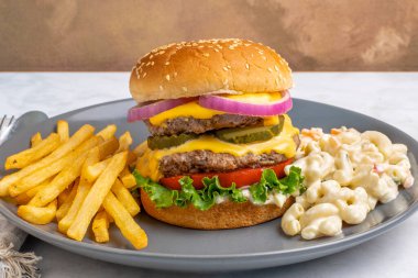 Çift peynirli burger, turşu ve soğanlı makarna salatası ve patates kızartması.