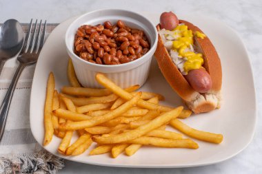 Sosisli sandviç, soğanlı ve hardallı fırında fasulye ve patates kızartması.